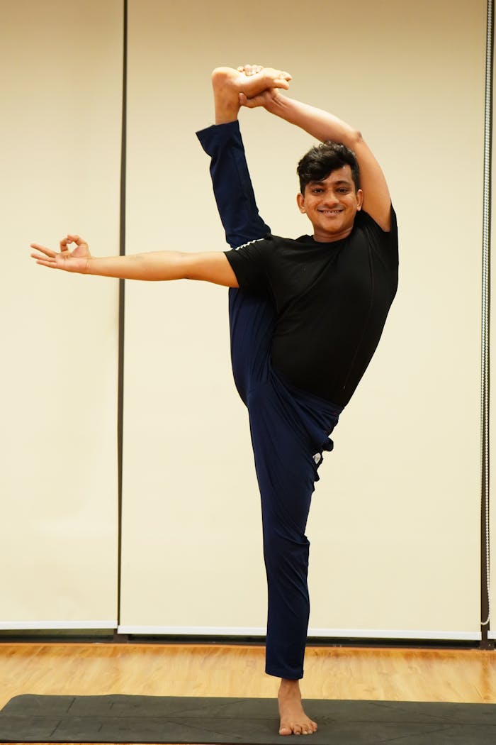 Young man demonstrating advanced flexibility and balance with yoga pose inside a studio.